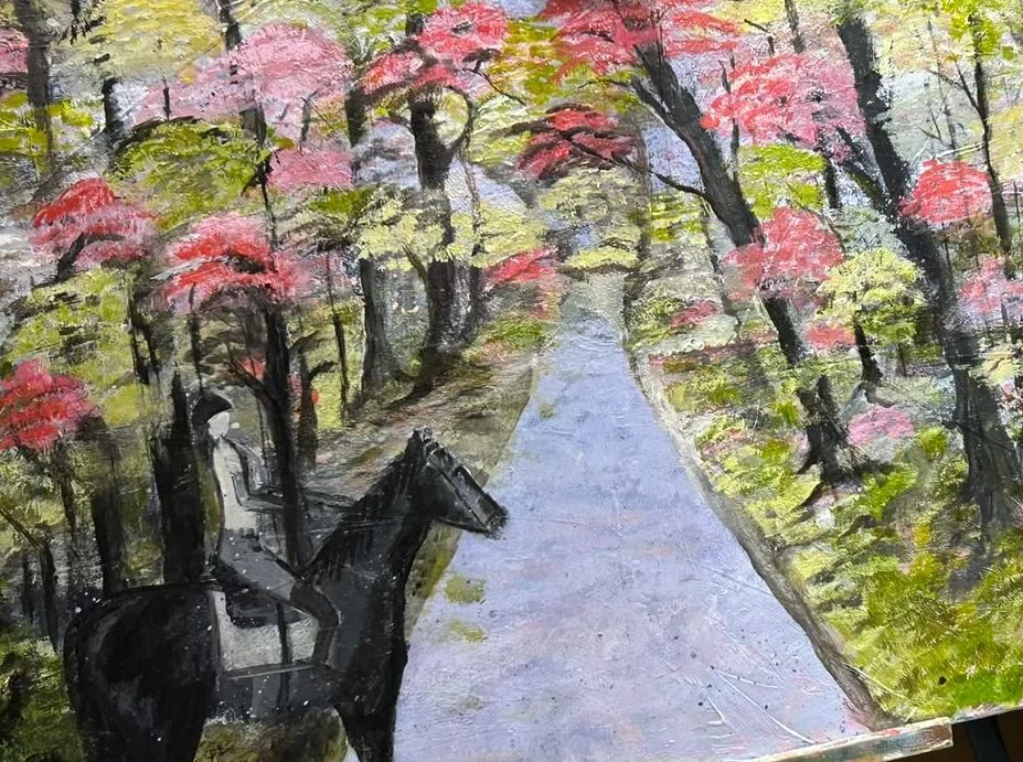A horse and rider pause beside a pale path that winds into a woodland of dark trees, pink blossoms and fresh green foliage.