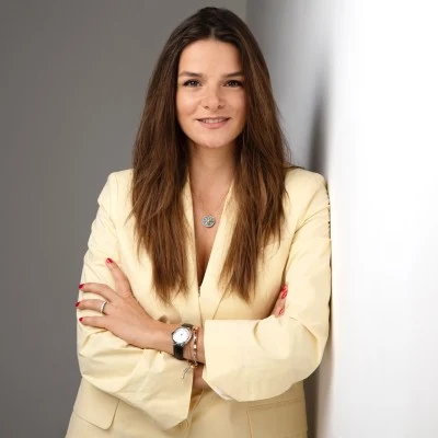 Artist Rania Hamdan, wearing a cream suit and standing beside a light wall